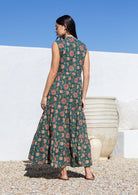 Woman wearing a floral cotton maxi dress standing against a white wall with blue sky.