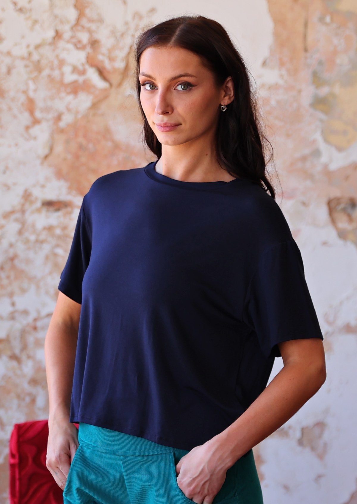 woman in navy blue rayon loose fit t-shirt  over teal corduroy pants with hands in pockets