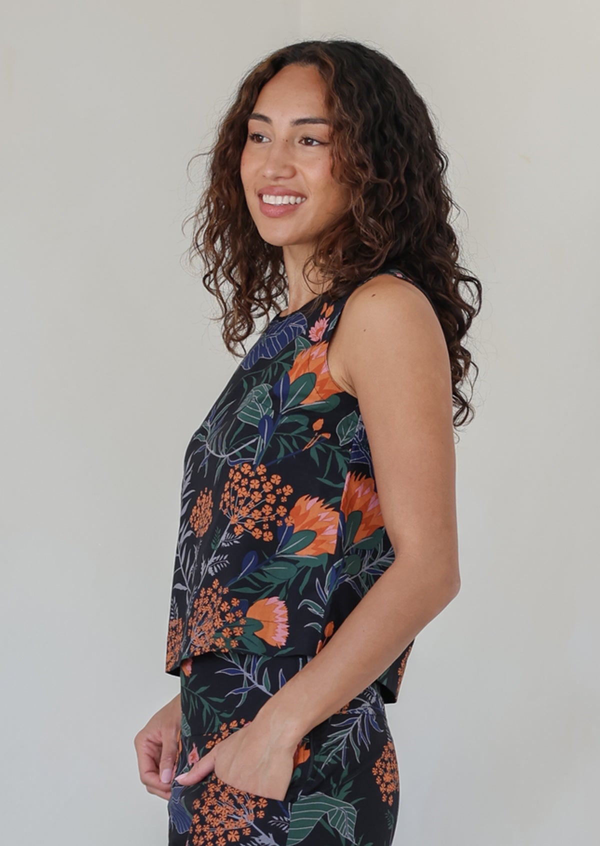 Woman stands sideways wearing a relaxed fit sleeveless cotton top with side bust darts and round neckline