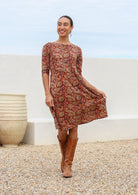 Model poses in midlength cotton dress with wide round neckline, 3/4 sleeves and pockets.