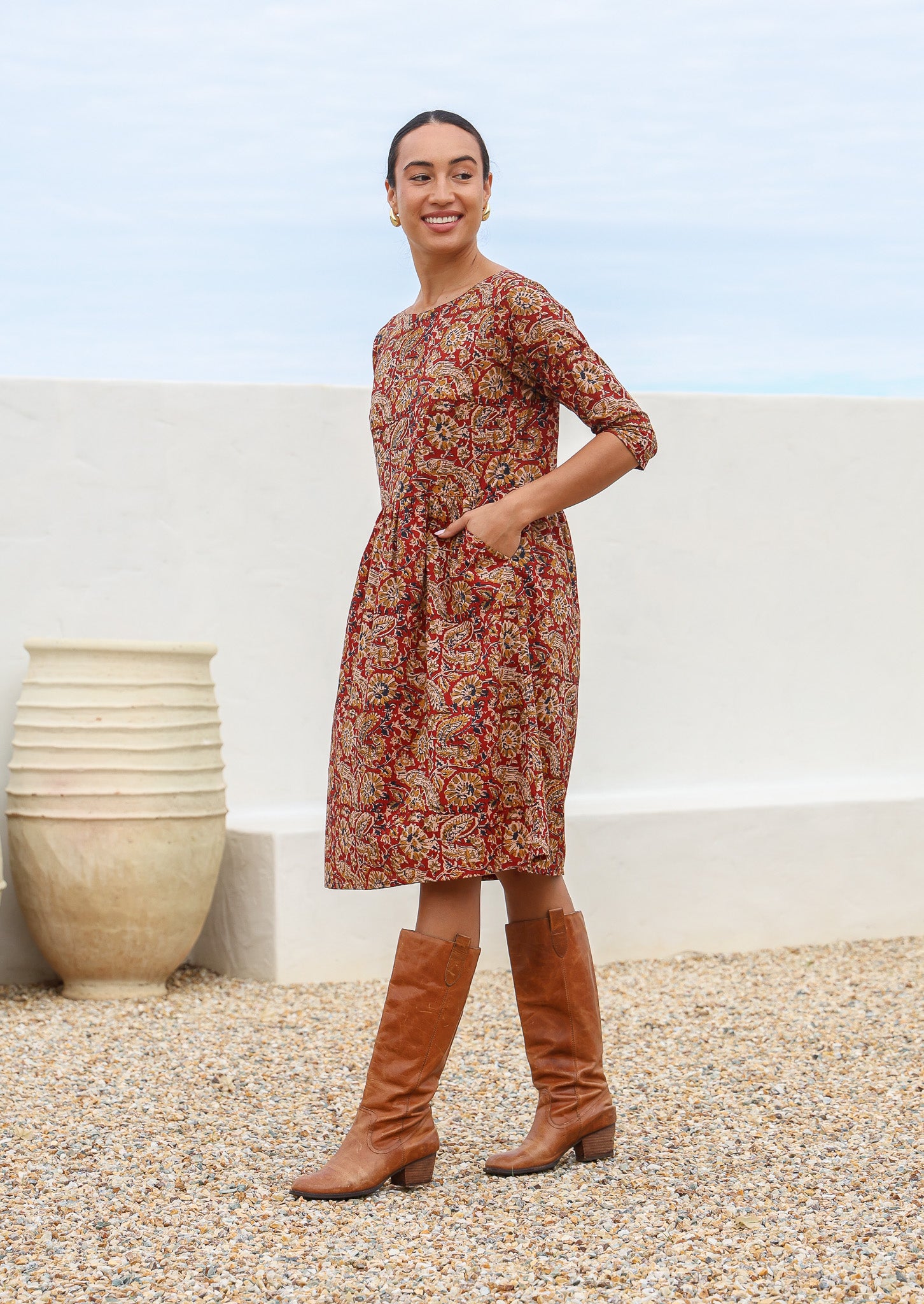 Model wearing relaxed fit, knee length cotton dress with wide round neckline and hands in pocket.