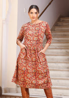 Model in knee length cotton dress with 3/4 sleeves, wide round neckline and hands in pocket.