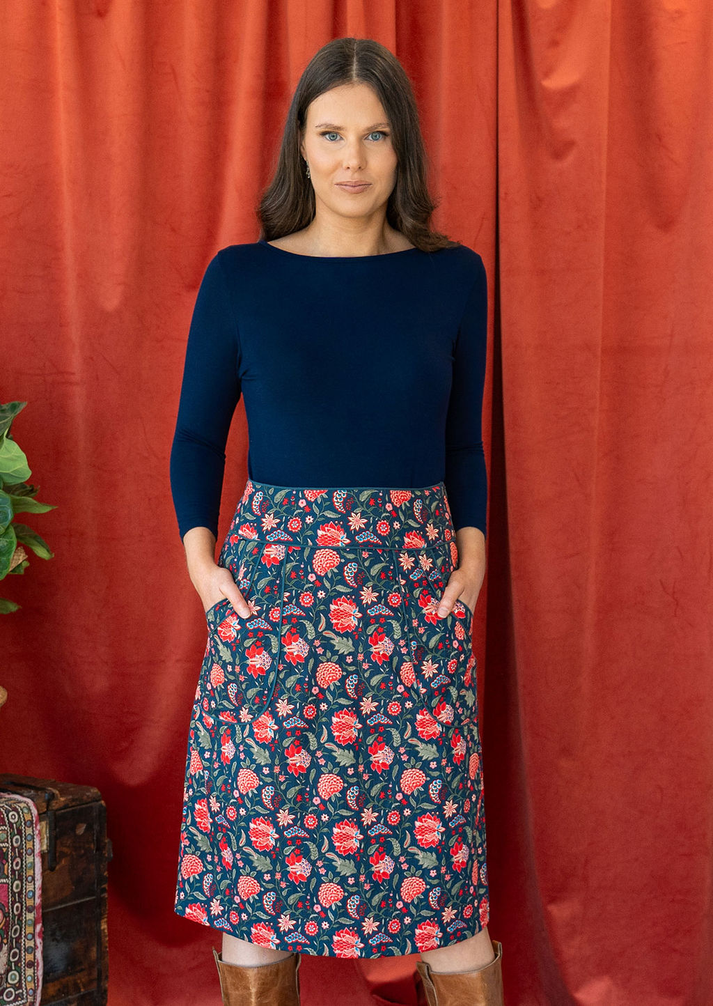Woman poses in cotton floral print knee length pencil skirt with hands in pockets, paired with a dark blue stretch rayon top