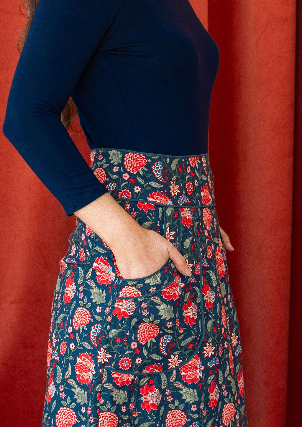 Close up of cotton red floral print on a blue base pencil skirt, with blue trim around the waistband and pockets