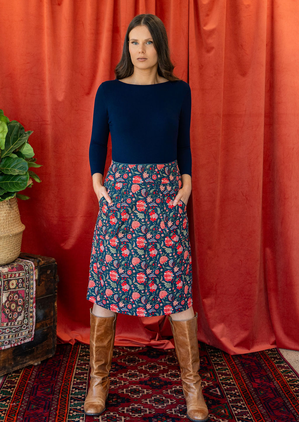 Model wears cotton floral print knee length pencil skirt with hands in pockets, paired with a dark blue stretch rayon top and tan boots