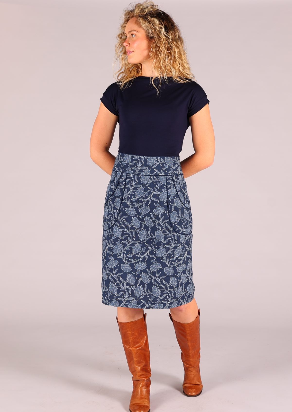 Model standing wearing Bridgette Neela navy blue cotton skirt paired with a navy Wide Neck Mod top and tan leather boots