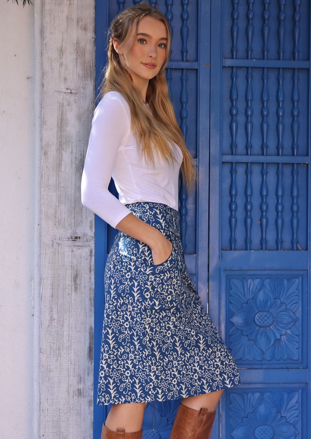 Woman stands sideways in blue based floral print cotton pencil skirt with side zip and pockets