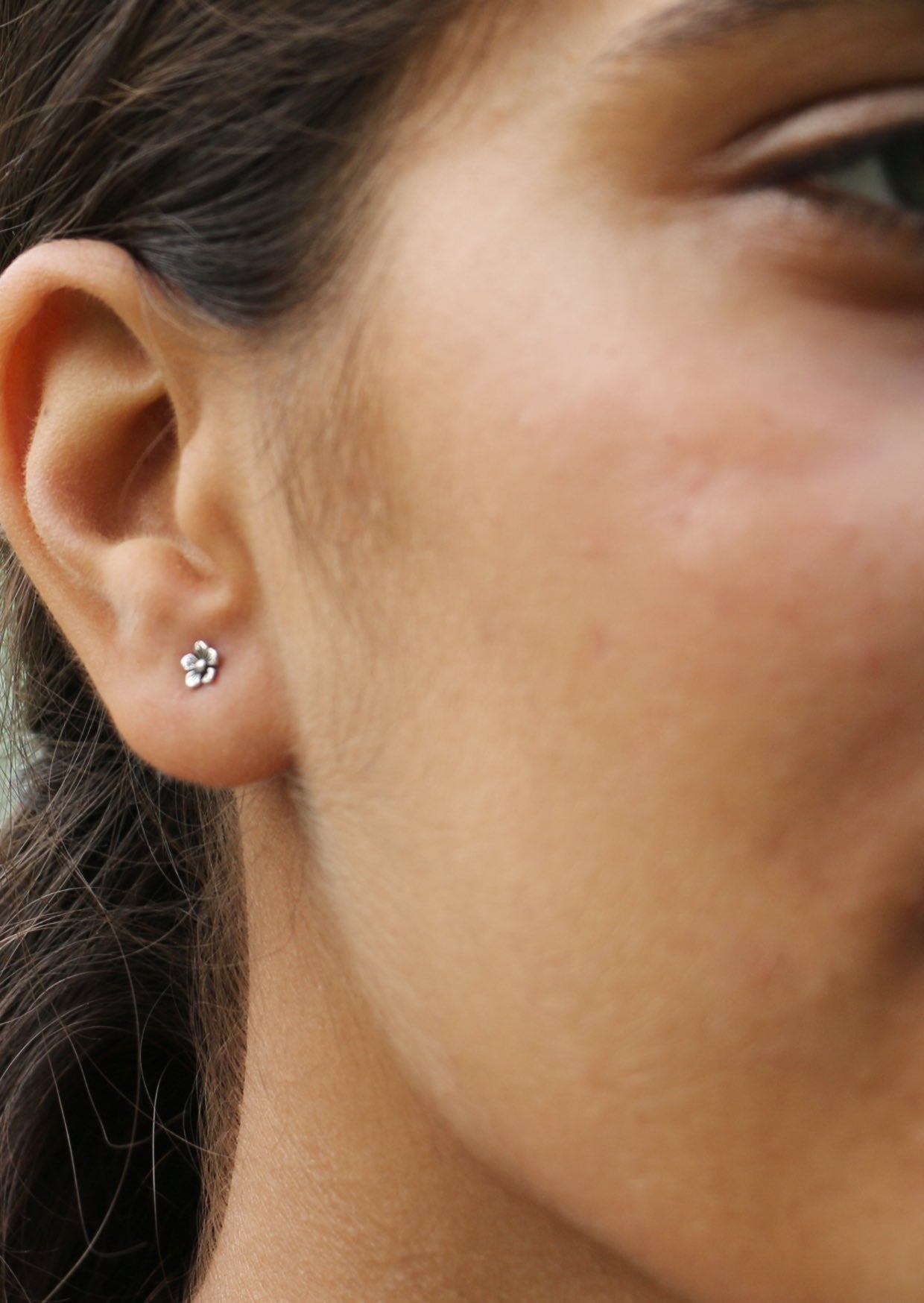 Woman wearing small buttercup studs with polished finish and charming flower design