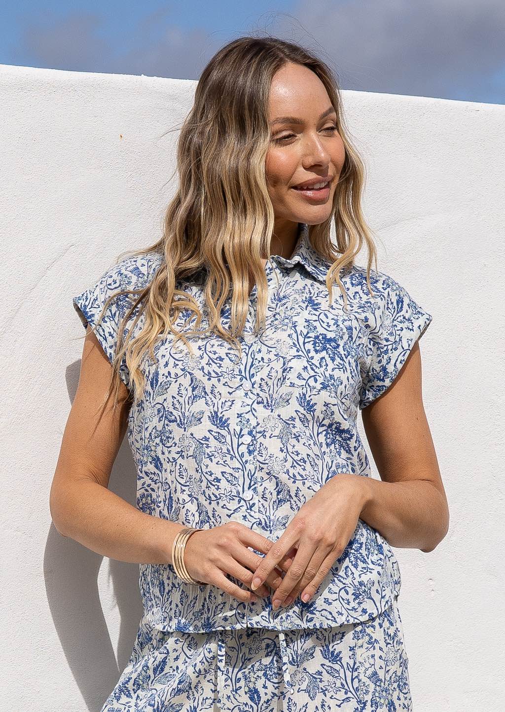 Woman wearing a white based blue floral print cotton shirt in a natural setting.
