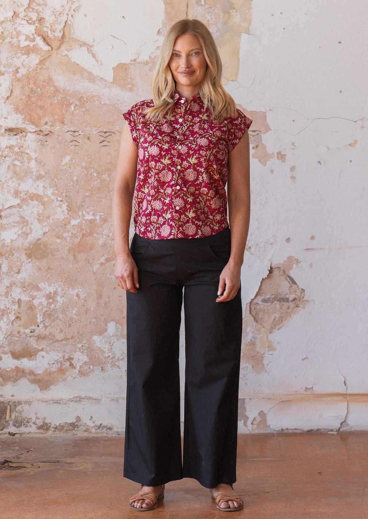 Woman stands in cotton floral print button through cap sleeved shirt paired with black cotton pants
