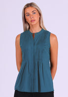 Model poses in blue sleeveless cotton top with high round neckline and tiny pleats across bust