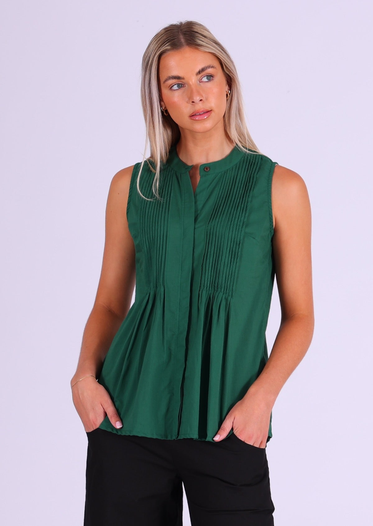 Model poses in deep green sleeveless cotton top with high round neckline and tiny pleats across bust