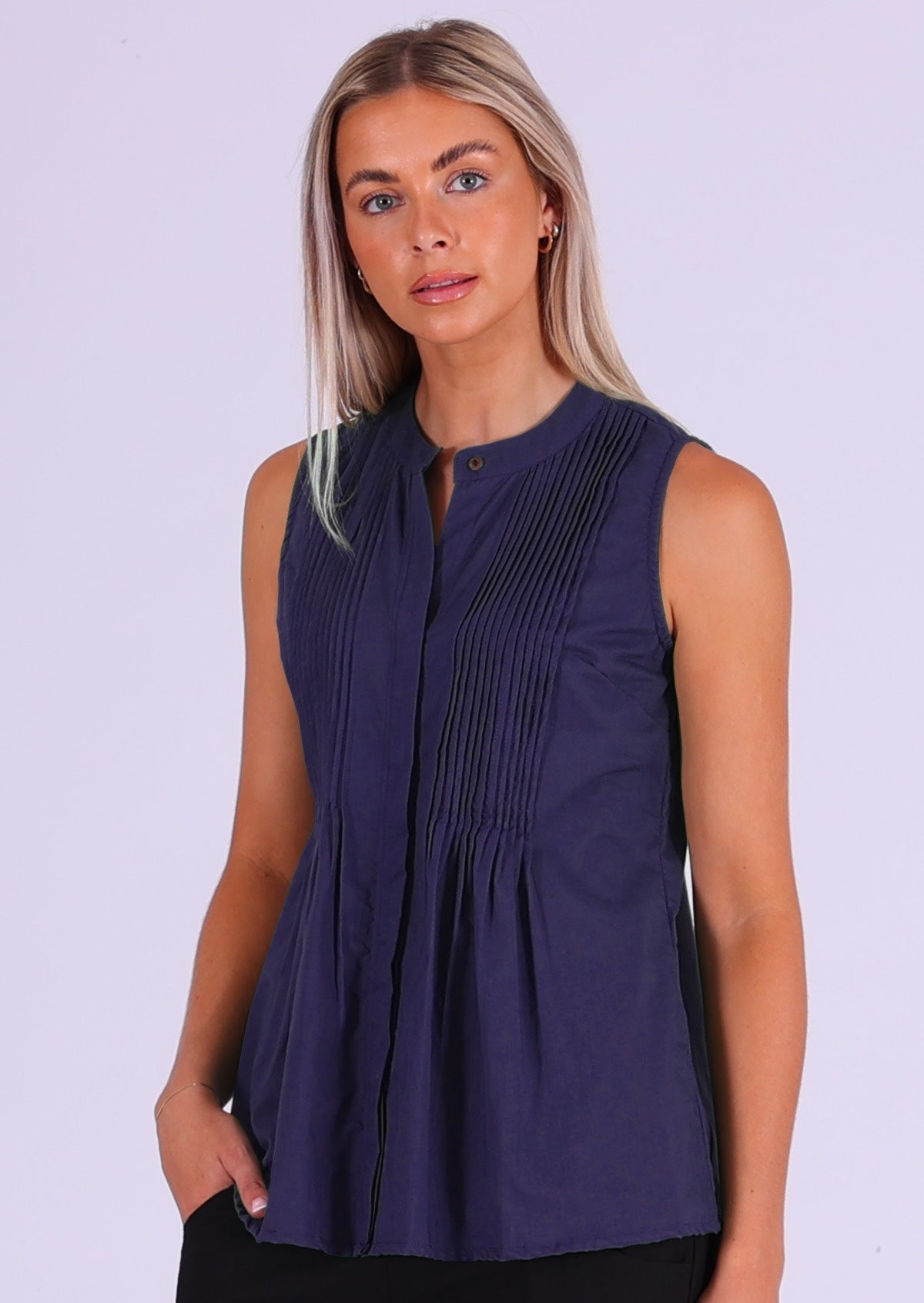 Model poses in dark blue sleeveless cotton top with high round neckline and tiny pleats across bust