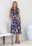 Woman wearing a navy floral sleeveless button through dress with a collar, with her hand in pocket