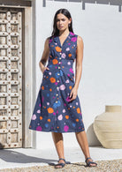 Woman wearing sleeveless, button through cotton dress with collar and pockets.