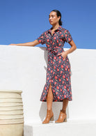 Model stands on side wears 100% cotton button through dress with short sleeves, removable waist tie and pockets.