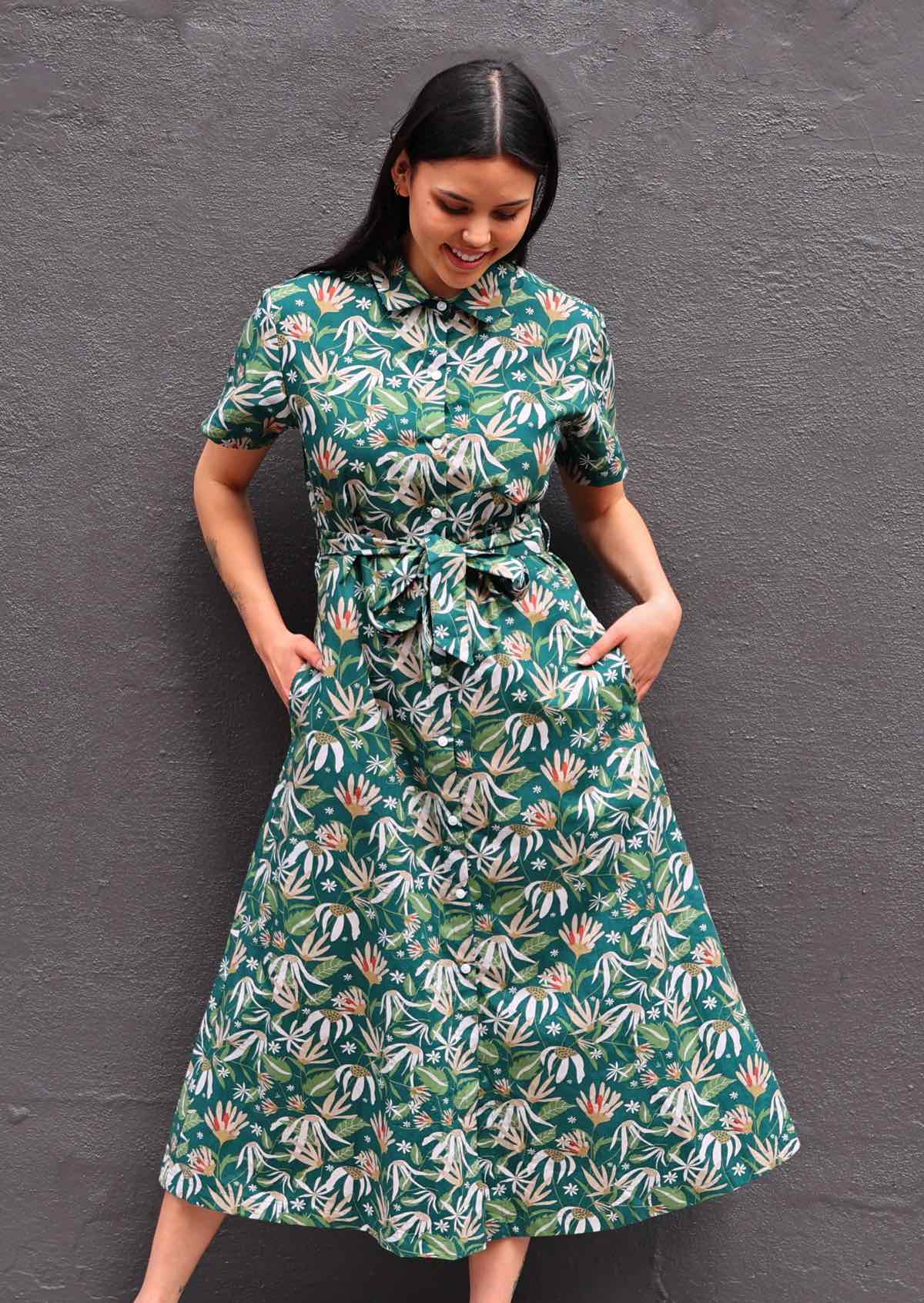 Woman with dark hair wearing 100% cotton green floral shirt dress, buttons up front, collar and pockets