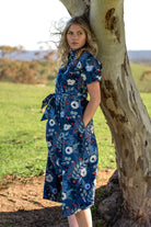 Chelsea dress gardenia print blue base 100 percent cotton shirt dress featuring pockets, waist tie, and collar paired with tan leather boots