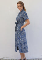 Woman stands side on in cotton shirt dress with short sleeves and collar, with her hand in side pocket