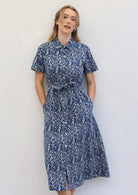 Woman wears cotton shirt dress with collar and T-shirt sleeves, with hands in hidden side pockets