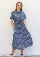 Woman poses in blue based floral print cotton shirt dress, holding skirt out to show its A-line shape