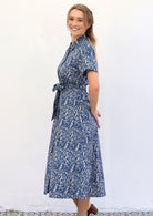 Woman stands side on in cotton shirt dress with short sleeves, collar and thick removable waist tie