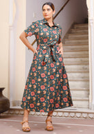 Woman wears 100% cotton button through shirt style dress with collar and short sleeves, in deep green based floral print.
