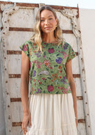 Woman wearing a moss green floral cotton top against a wooden door.