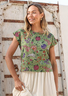 Woman wearing a moss green floral cotton top against a wooden door.
