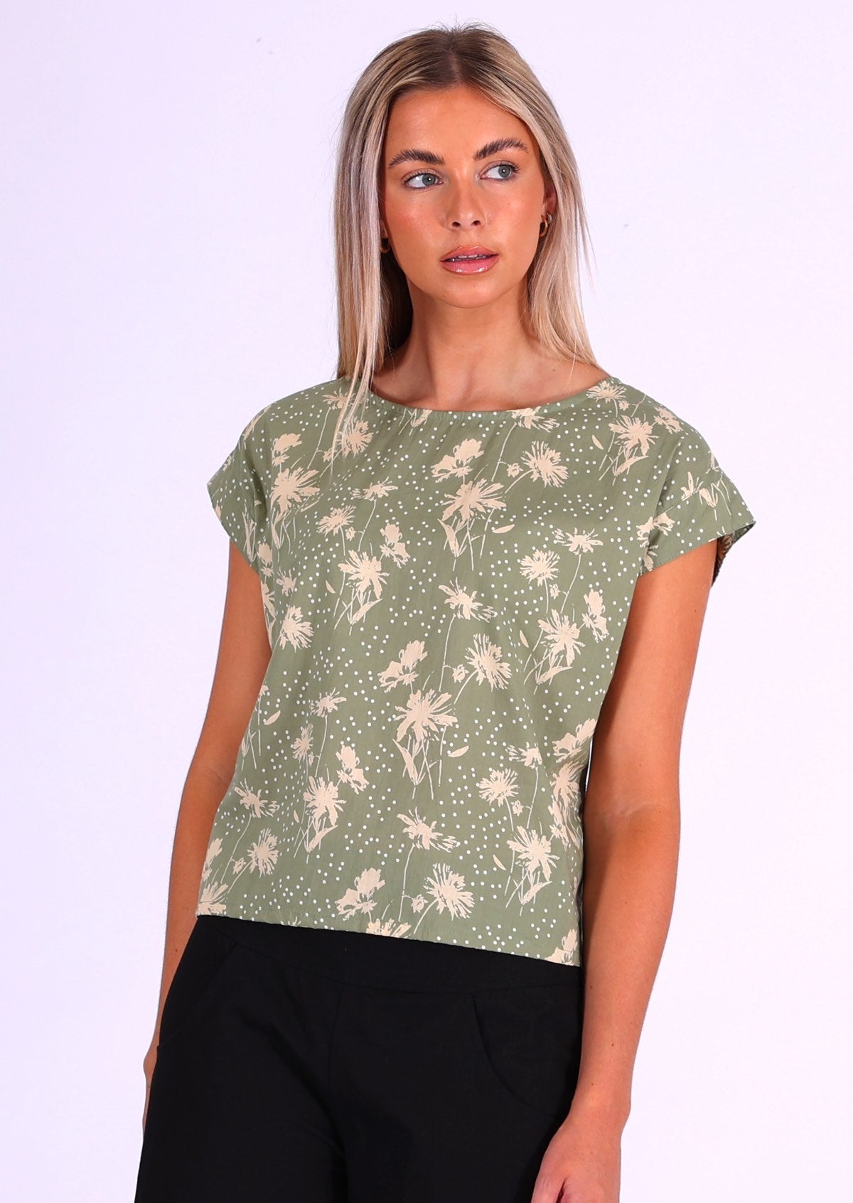 Woman stands in cotton cap sleeved top with high round neckline, in pale green based, cream floral print