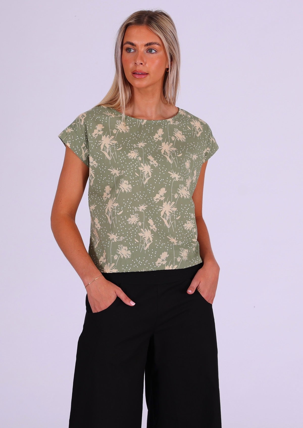 Woman wears cotton short sleeve top with sweet, cream coloured floral silhouettes and white spots on a pale green base