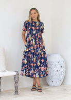 Woman wears relaxed fit, three tiered midlength dress with round neckline, short sleeves and pockets.