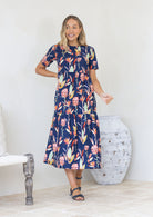 Model wearing short sleeved pink and green floral print navy cotton dress with pockets and round neckline.