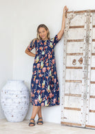 Woman in a relaxed fit floral navy blue cotton dress standing next to a decorative wooden door.