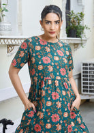 Model in green floral print dress with round neckline, short sleeves and hands in pocket