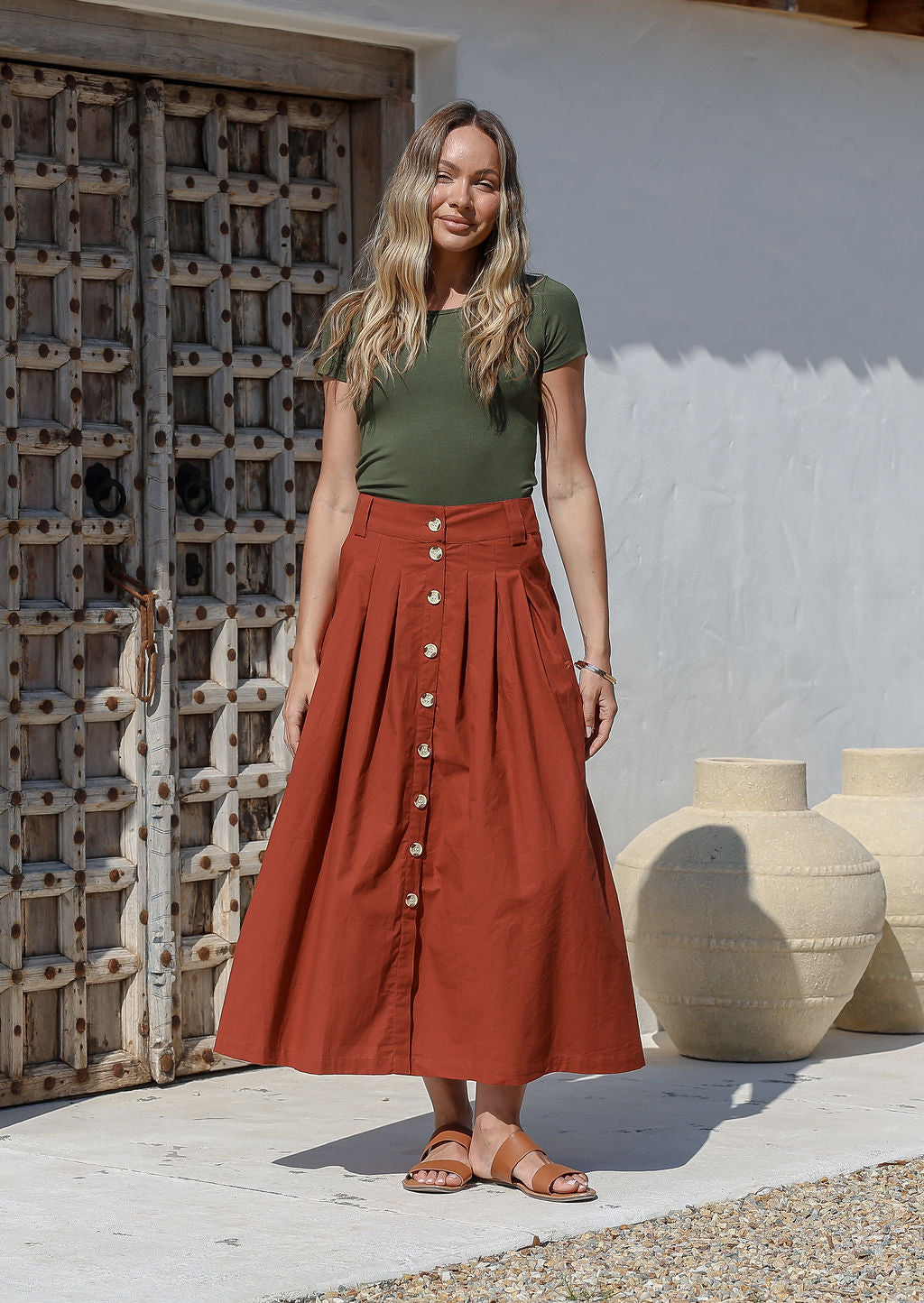 Woman standing in front of the wooden door wears 100% cotton button through  A line maxi skirt with belt loops and box pleats