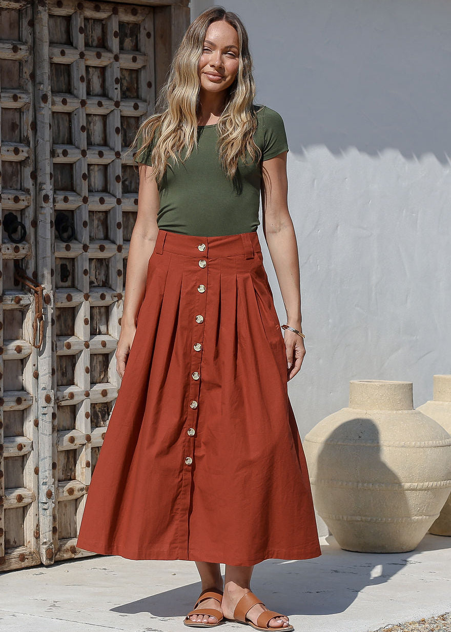 Woman standing in front of the wooden door wears 100% cotton button through A line maxi skirt with belt loops and box pleats