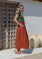 Woman wearing basic olive green top paired with cotton button through a-line skirt with box pleats and pockets in burnt henna shade