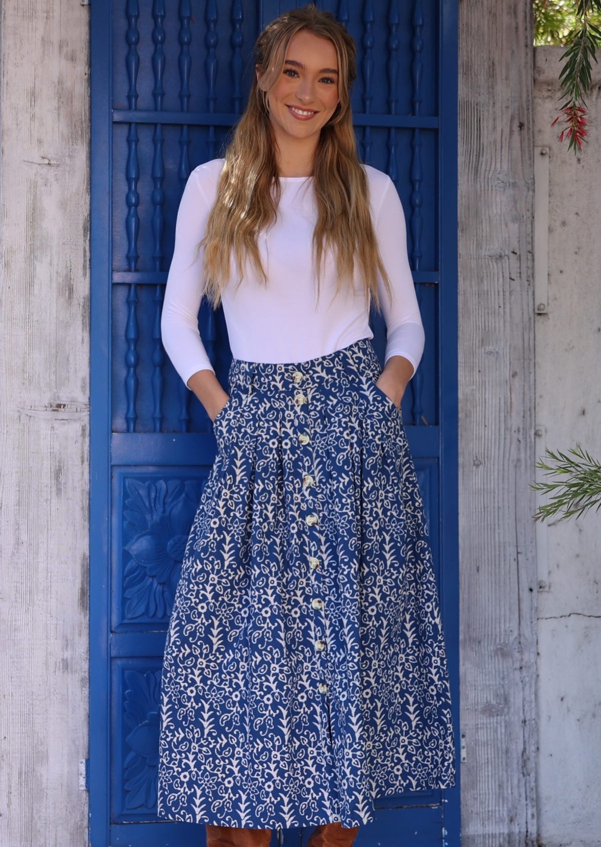 Woman wears blue based white floral print cotton button through skirt with hands in pockets