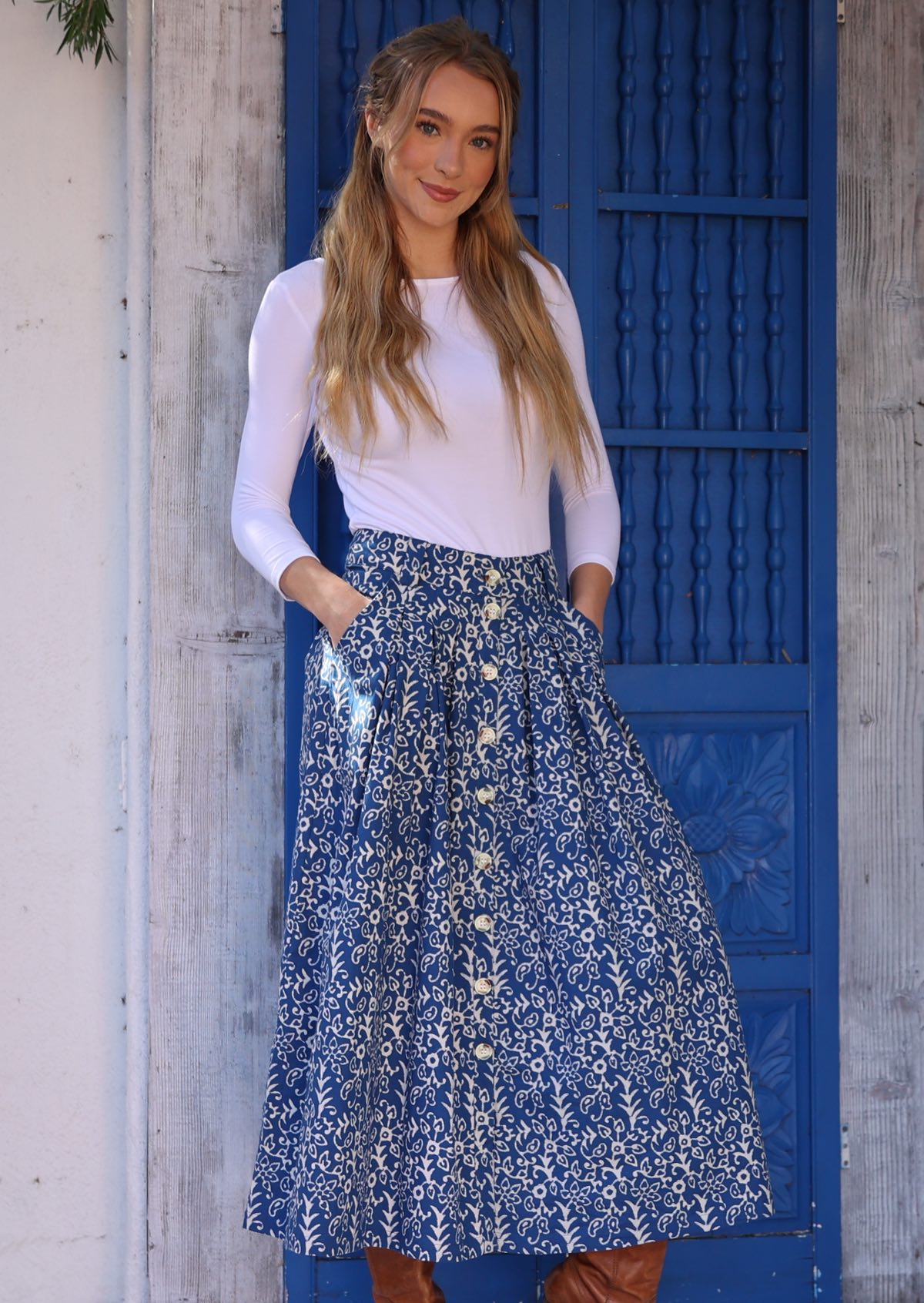Model poses in a midi length button through skirt with belt loops and box pleats with her hands in pockets