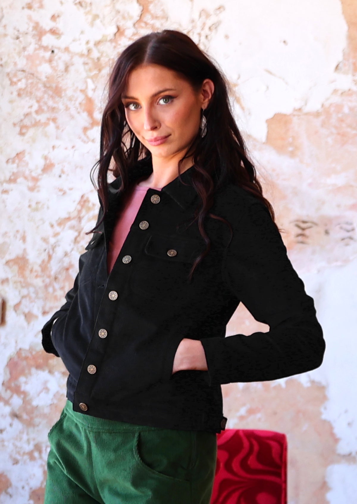 Woman wearing long sleeve cotton corduroy jacket with brass buttons and pockets over green corduroy pants