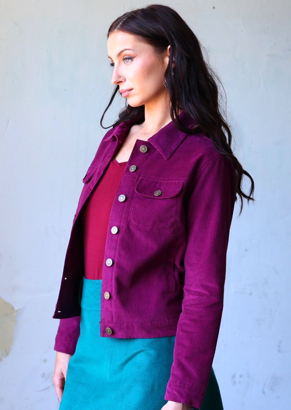 Woman wearing 100% cotton purple corduroy jacket with breast and front pockets, and brass buttons