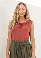 Woman wearing a terracotta coloured sleeveless singlet top with a cowl neckline