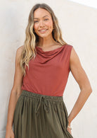 Woman wearing a terracotta coloured sleeveless top and olive green skirt against a white background