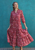 Model poses in deep bright red floral print cotton tiered maxi dress, holding skirt out to show volume