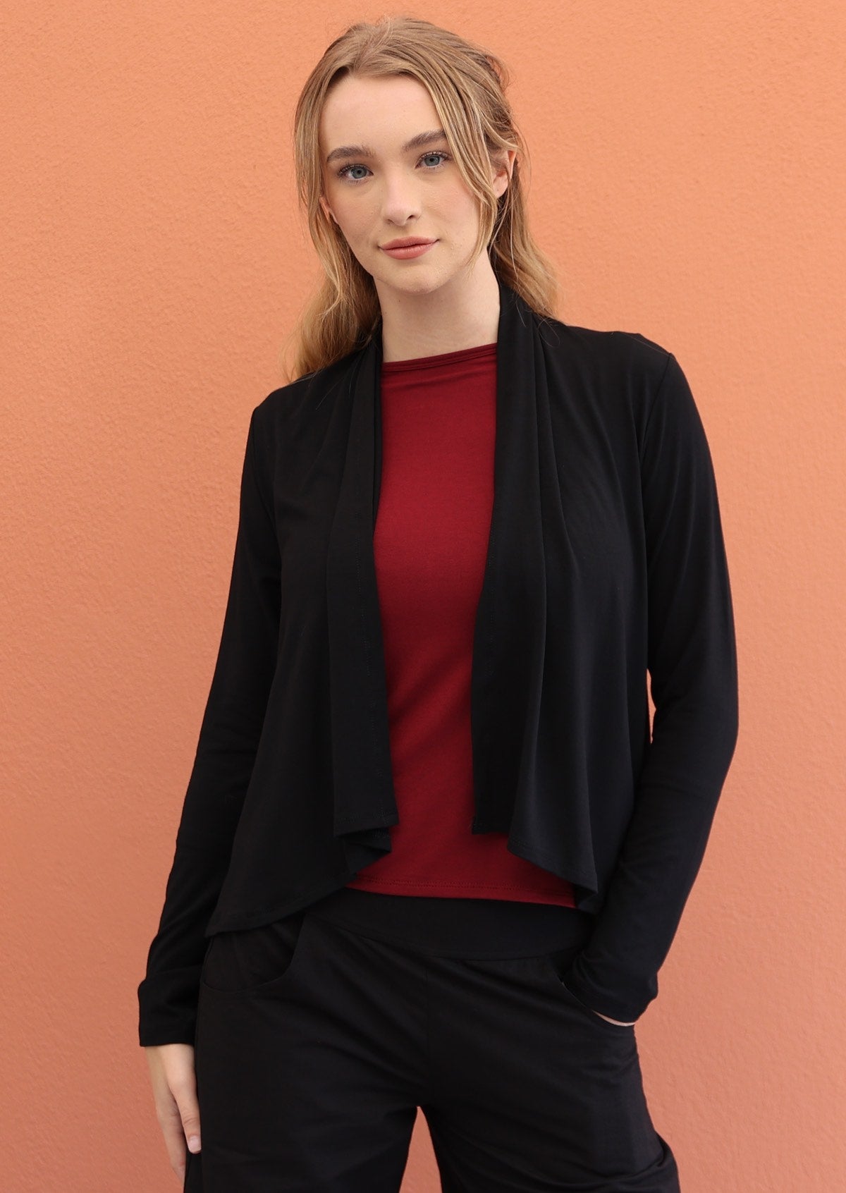 Woman wears black long sleeve stretch rayon cardi with a waterfall front hem that is cropped at the front