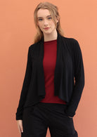 Woman wears black long sleeve stretch rayon cardi with a waterfall front hem that is cropped at the front