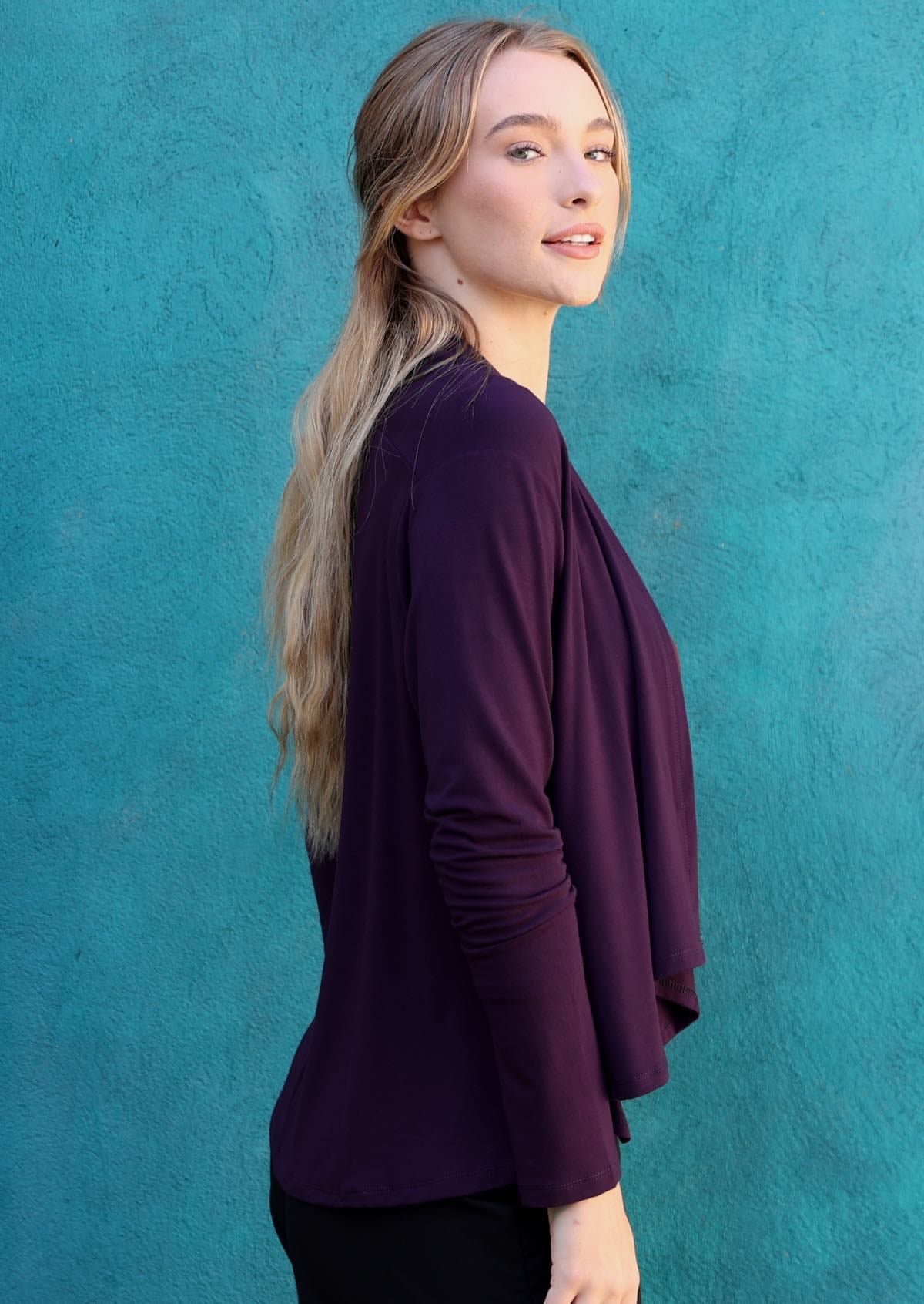 Model wears dark purple long sleeve stretch rayon cardi that is longer at the back, with black pants