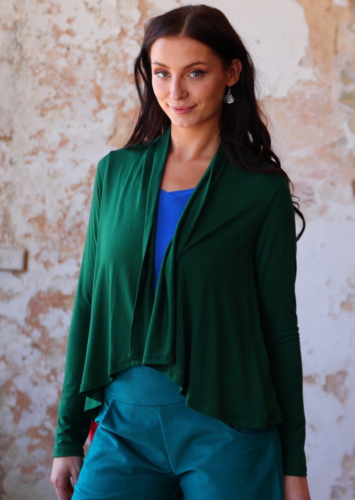 Woman wears forest green long sleeve stretch rayon cardi with a waterfall front hem, that is longer at the back