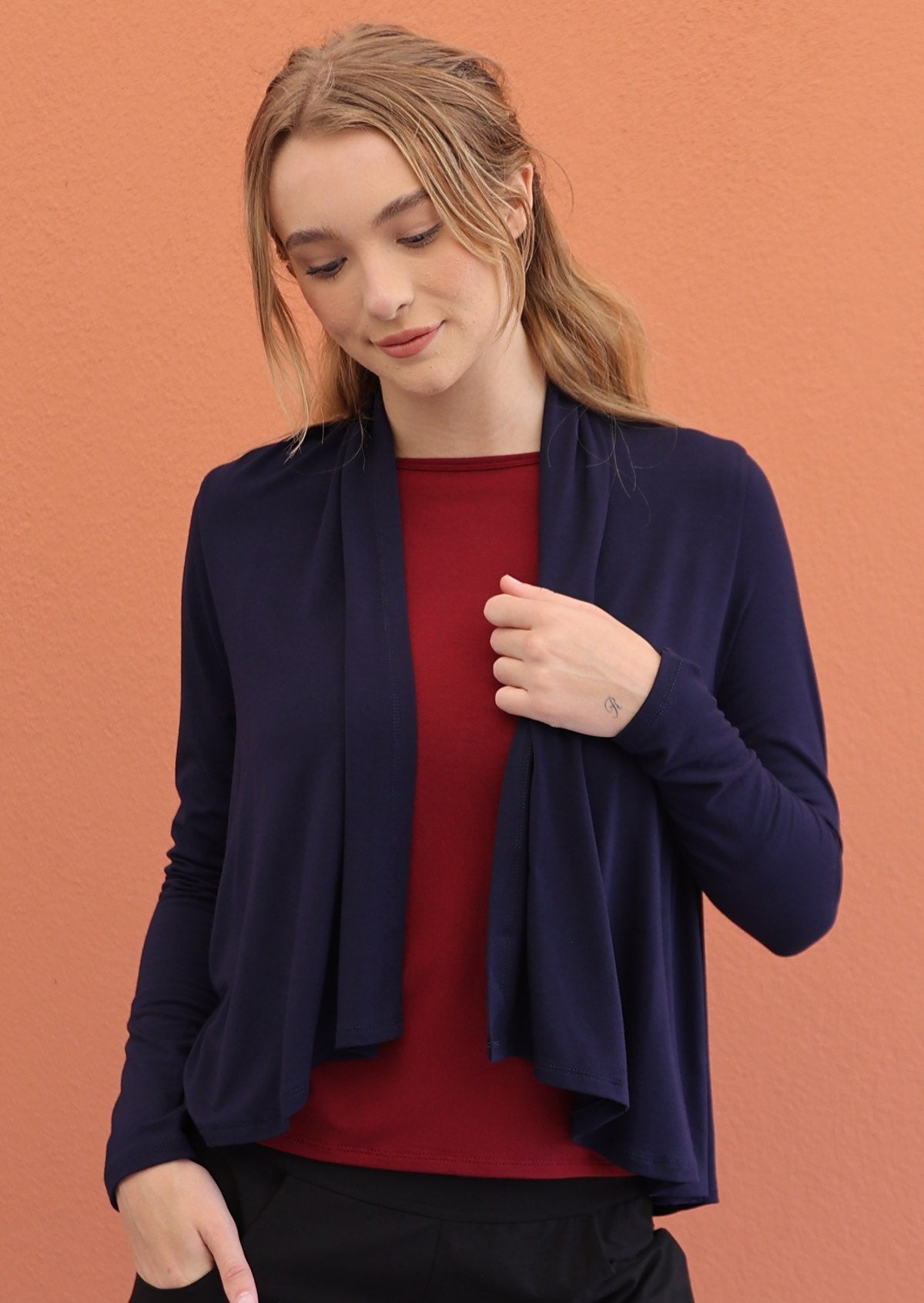 Woman looks down, in navy blue long sleeve stretch rayon cardi with waterfall front hem that exposes maroon top underneath